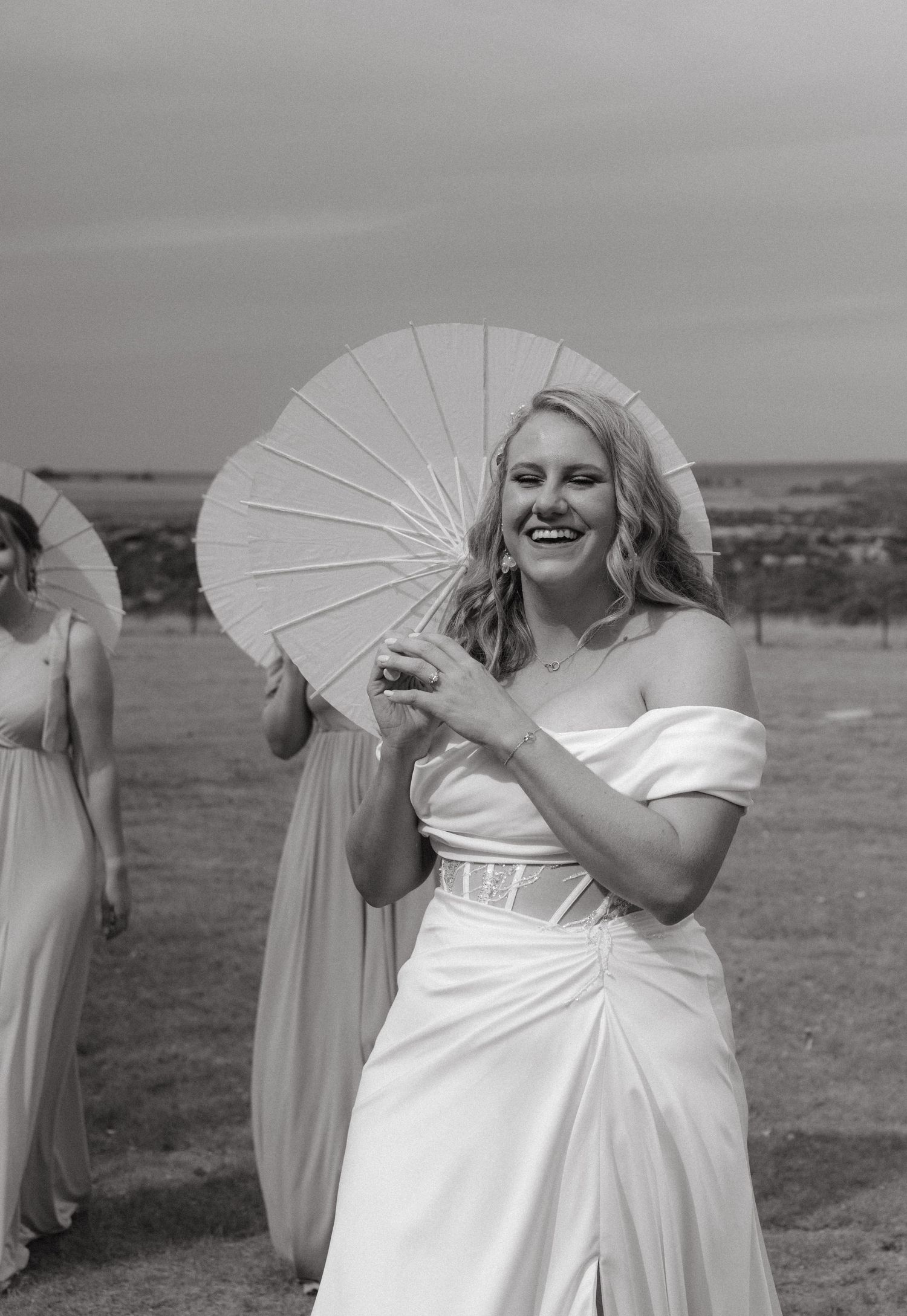 Black and white photo of bride holding white parasol outdoors with elegant dress.