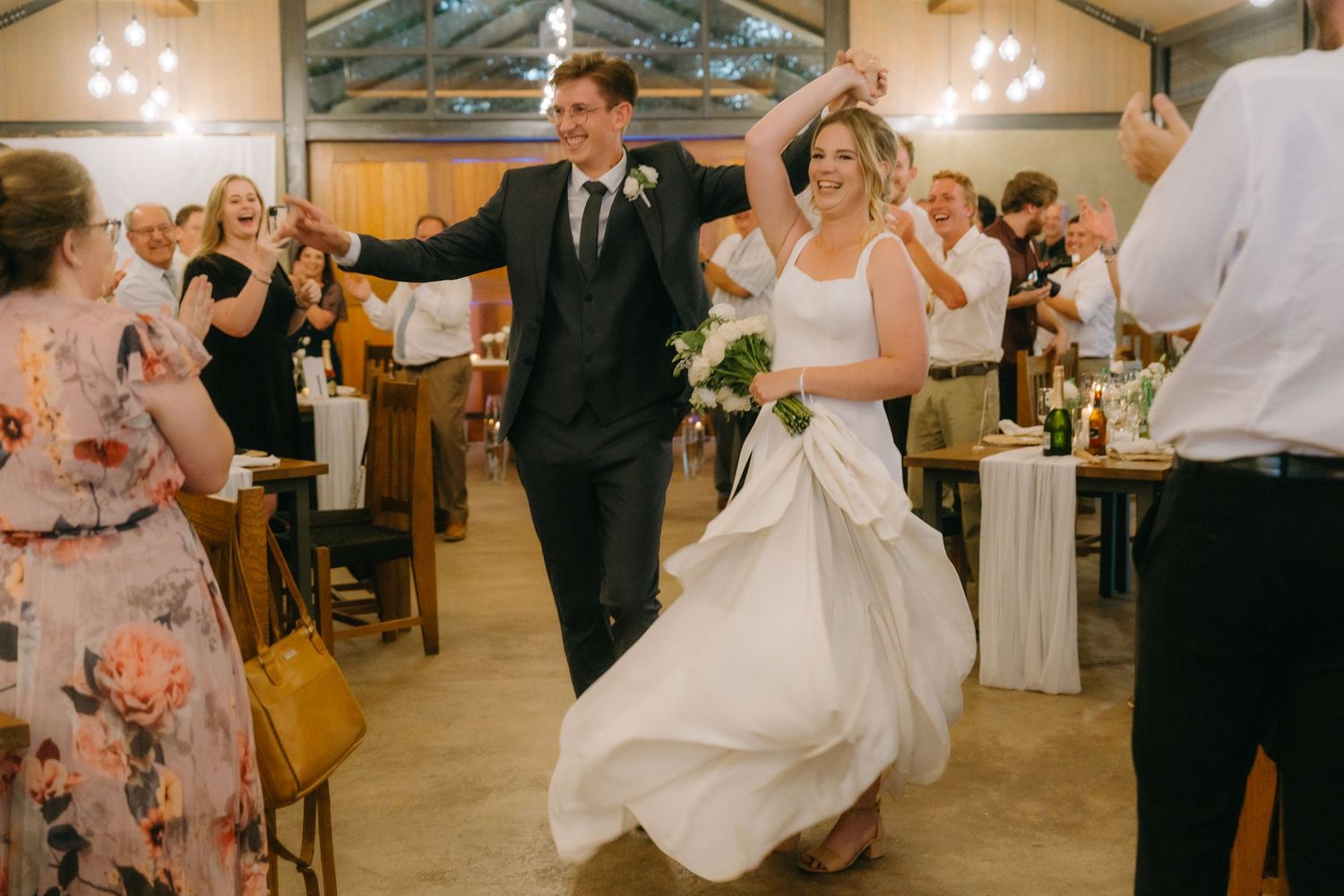 Newlyweds dance joyfully together on the dance floor at their rustic indoor wedding reception.