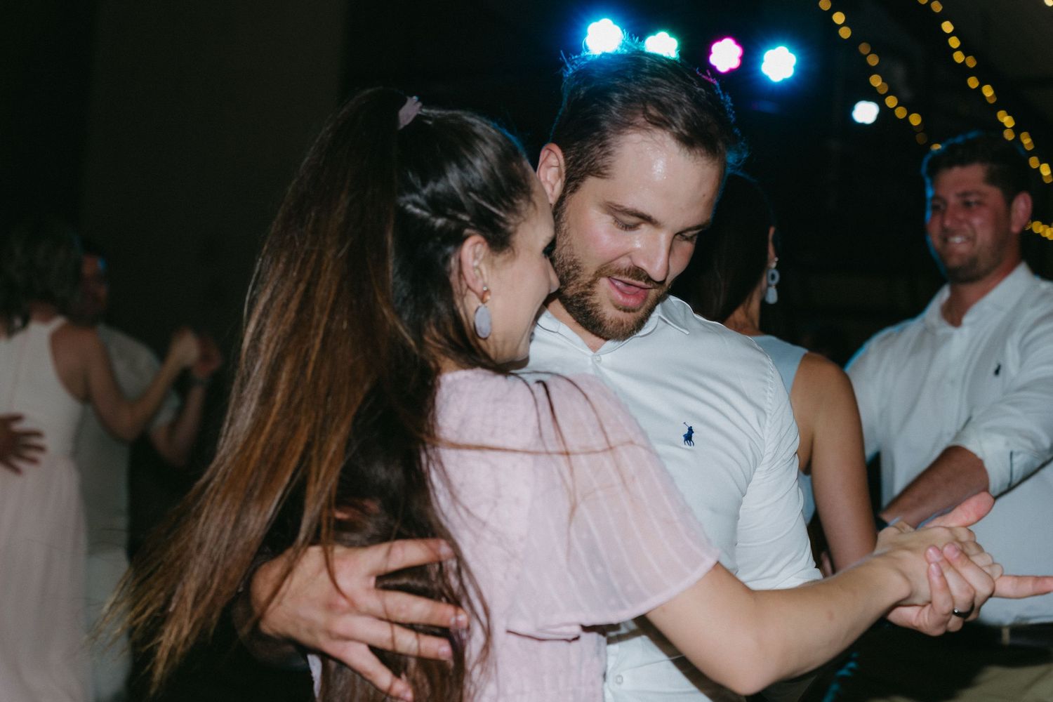 Couple dancing together at night event with lights and crowd in background.