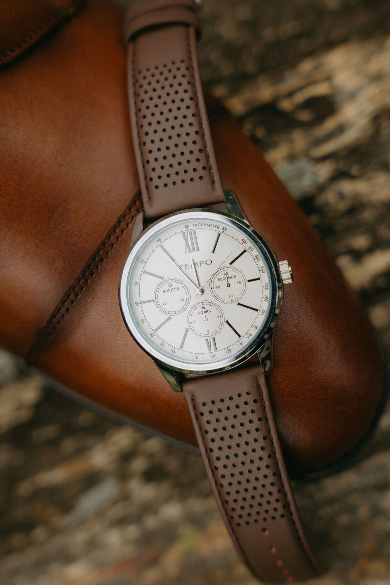 Elegant watch with brown leather strap and white dial displayed on textured surface.