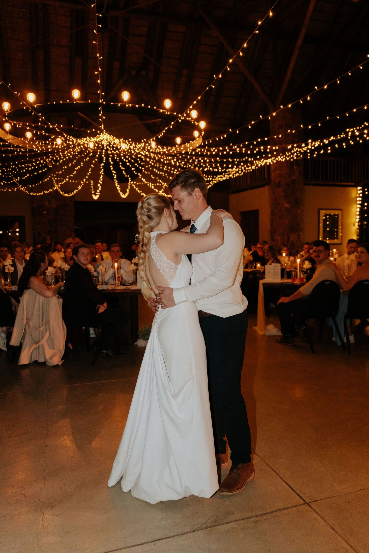 Couples dancing under warm string lights at an indoor wedding reception.