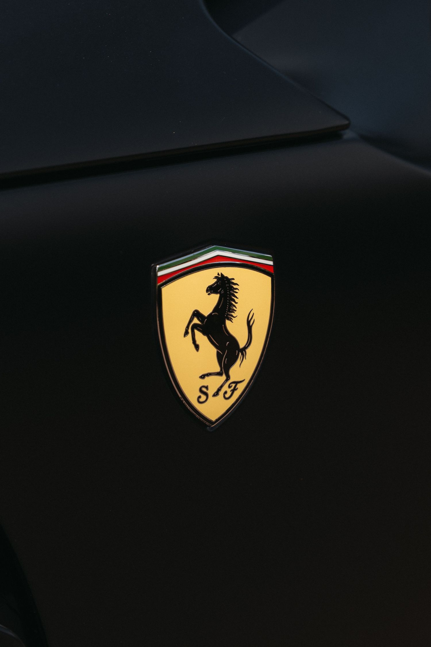 The iconic Ferrari prancing horse logo emblem in yellow and black against a dark background.