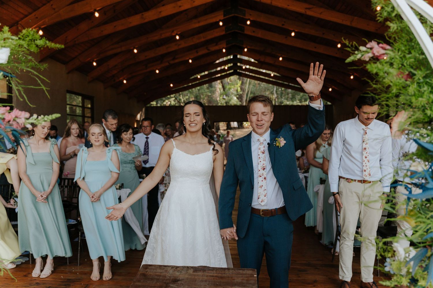 Joyful wedding celebration inside a rustic wooden barn venue decorated with greenery and twinkling lights.
