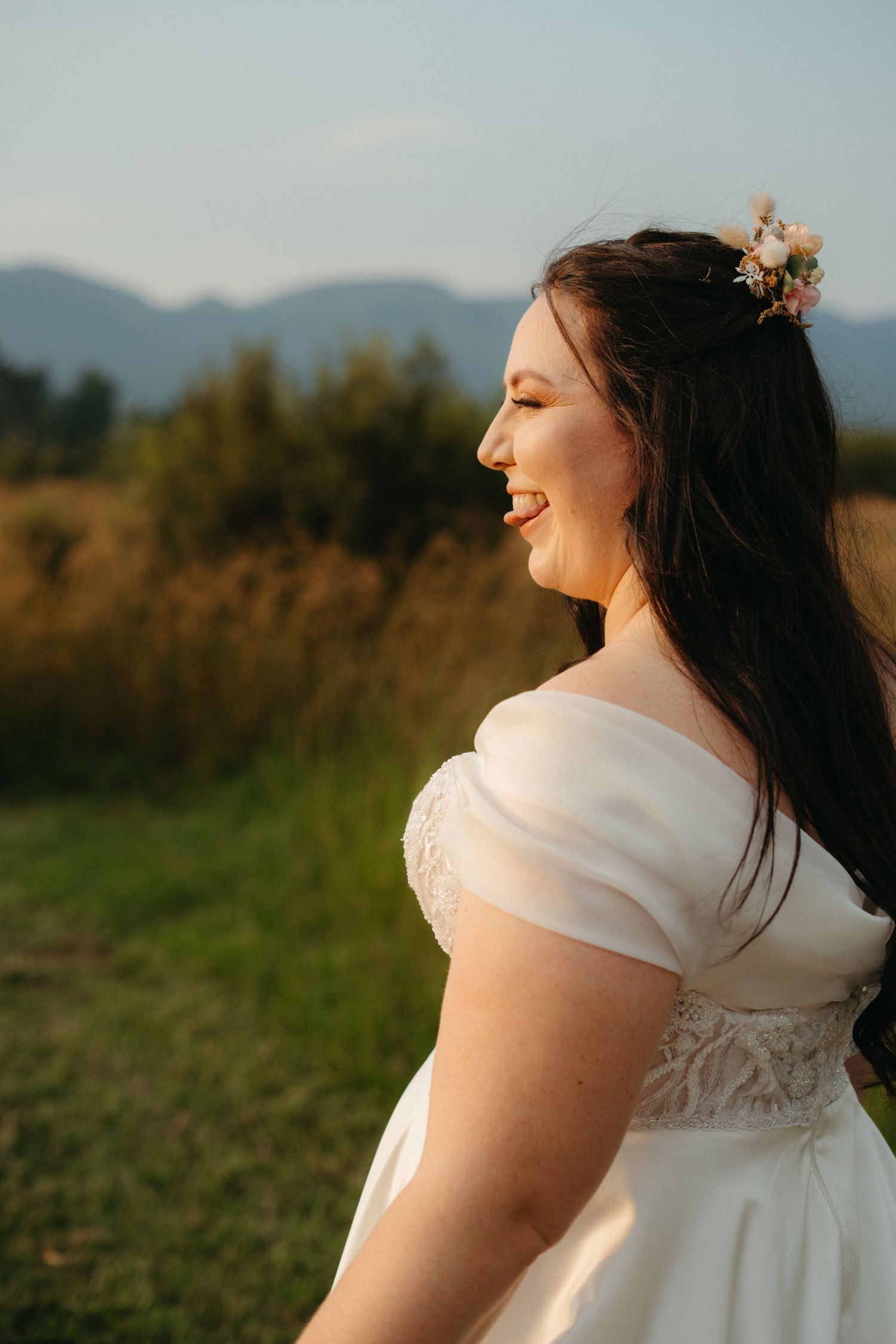 Golden hour portrait of joyful bride in classic white gown against mountain landscape.