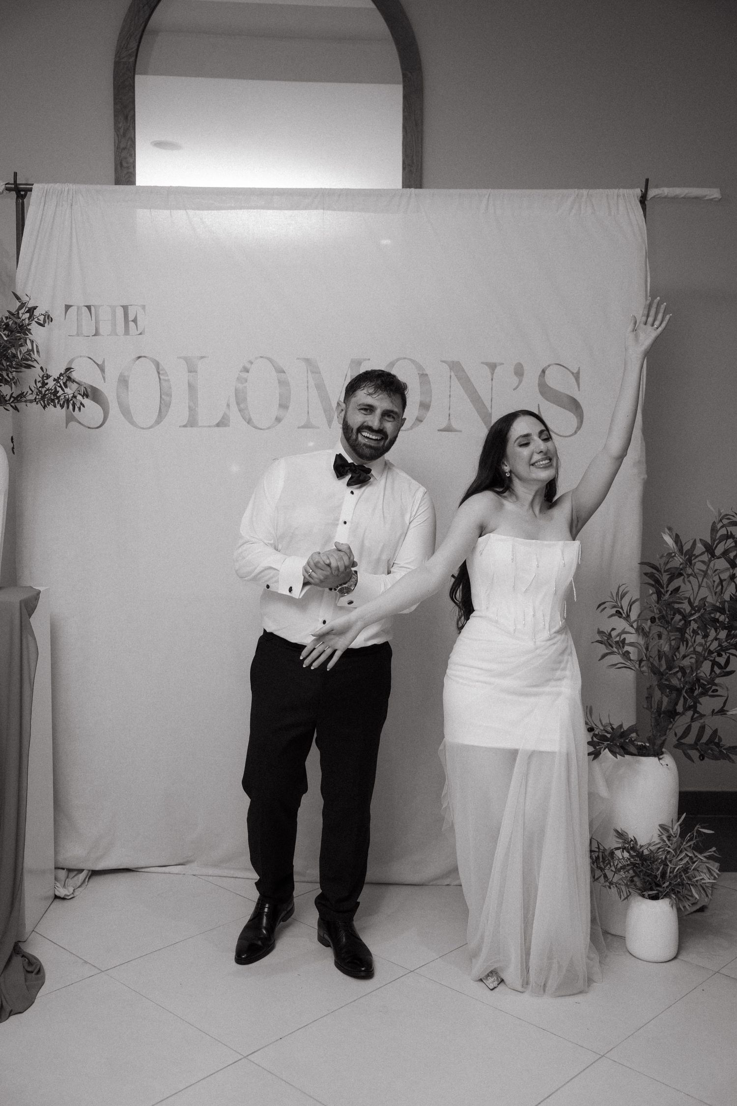 Black and white photo of newlyweds celebrating in front of The Solomons wedding backdrop.