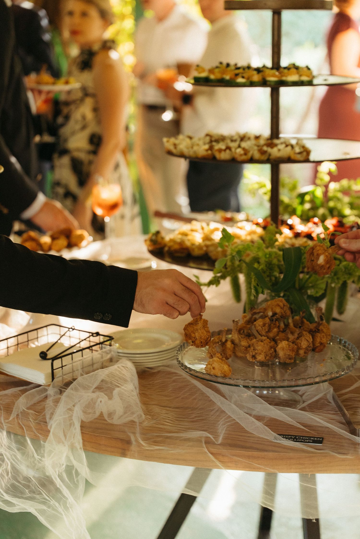 Hand reaching for fried appetizers at an elegant wedding catering display with tiered trays of hors d'oeuvres.