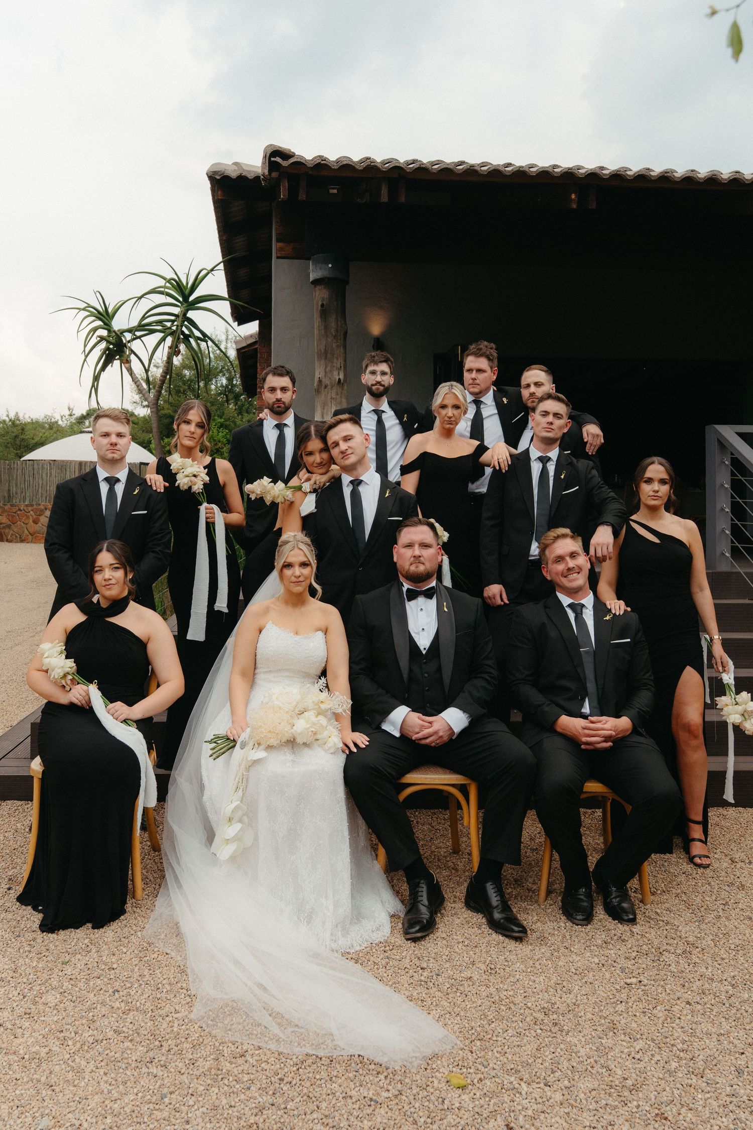 Wedding party in formal black attire and white gowns posed together on outdoor patio.