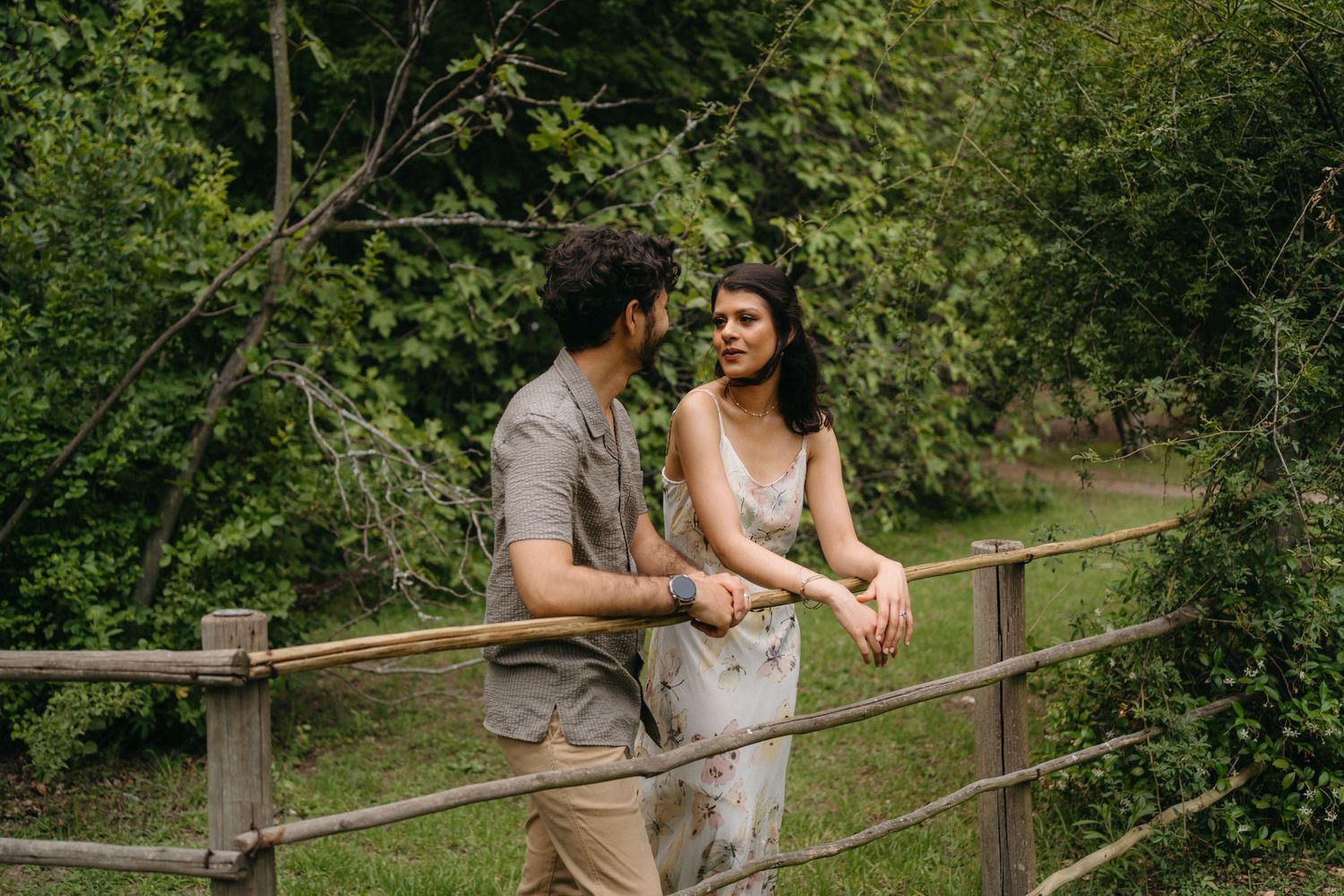 Couple sharing a romantic moment while leaning on wooden fence in nature.