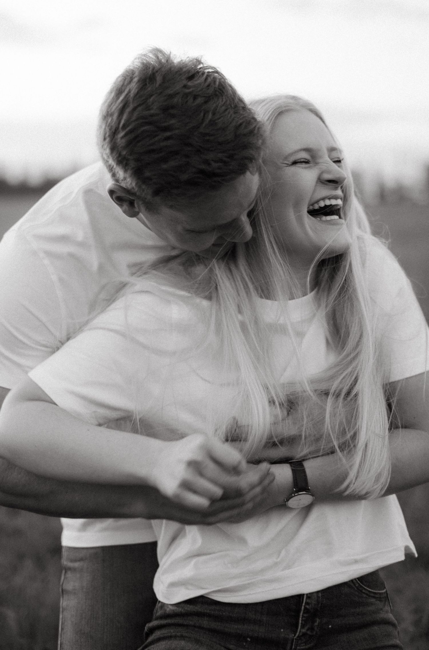 A heartfelt black and white candid moment showing a joyful couple in white t-shirts embracing and laughing together.