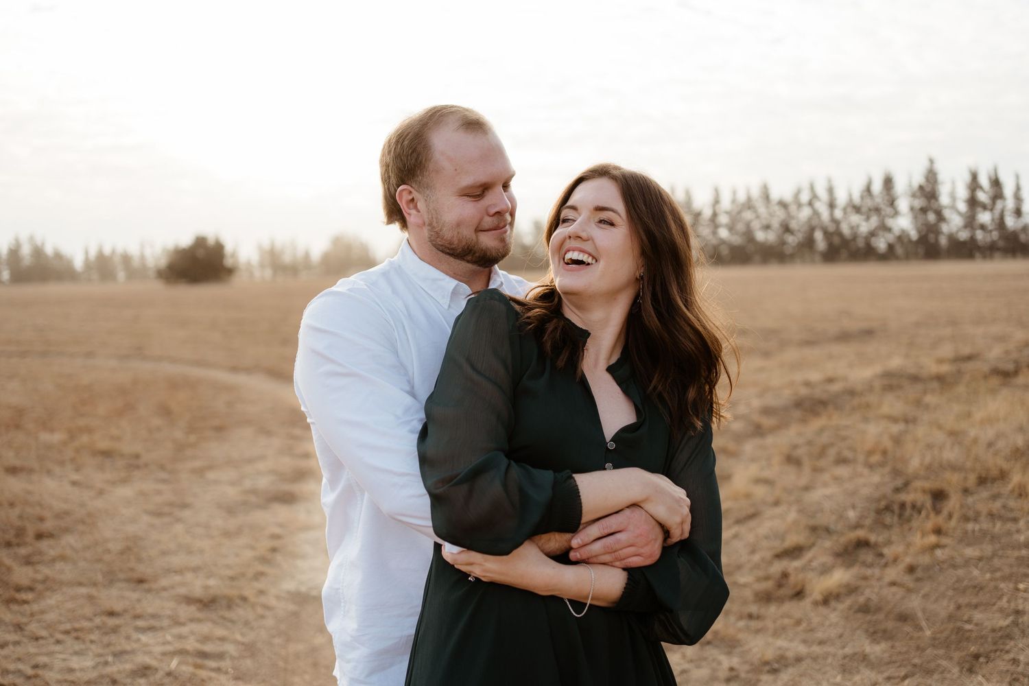 A couple laughing and embracing in a field during sunset.