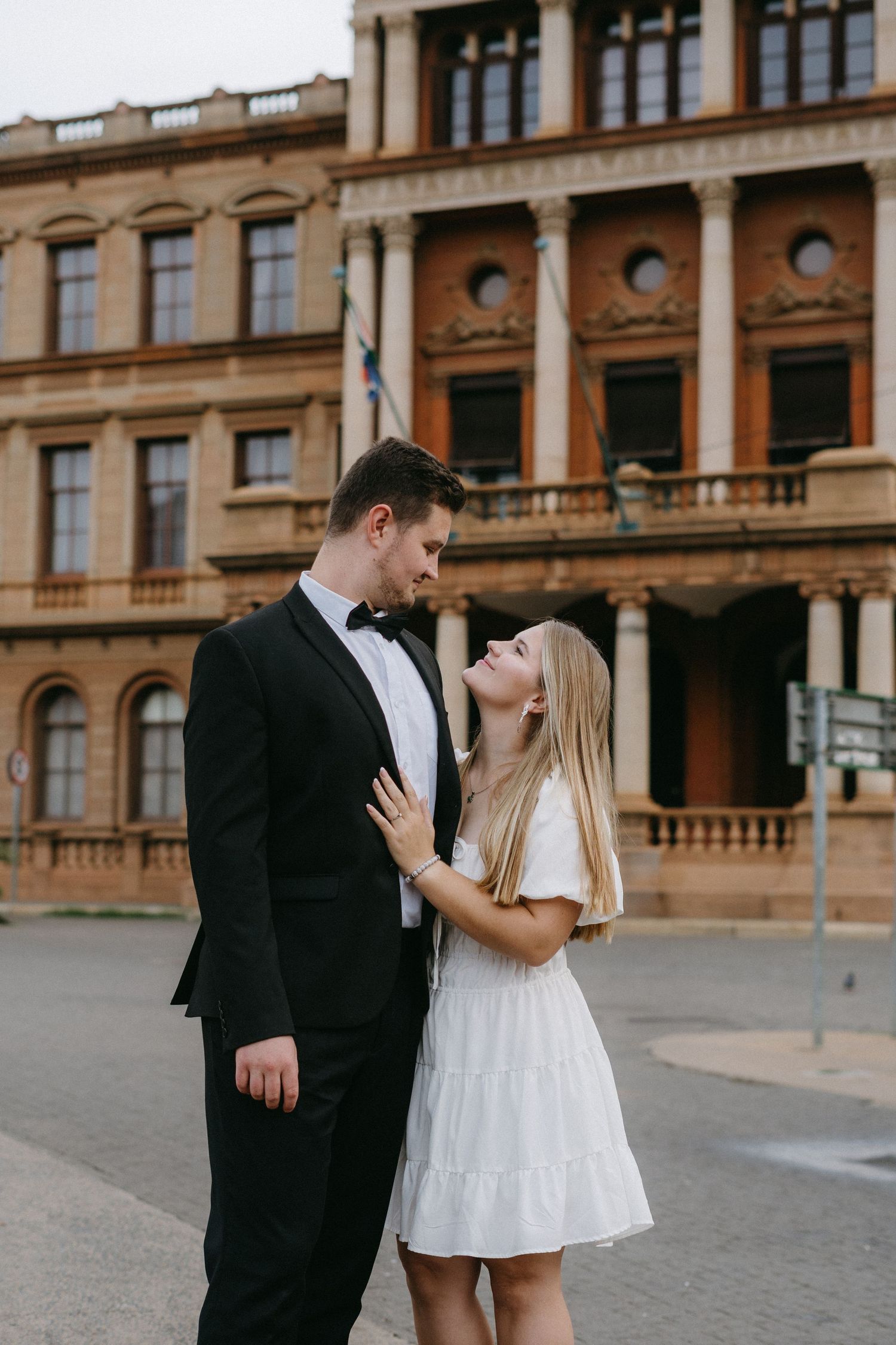 Romantic couple in formal attire sharing an intimate moment in front of a historic sandstone building.