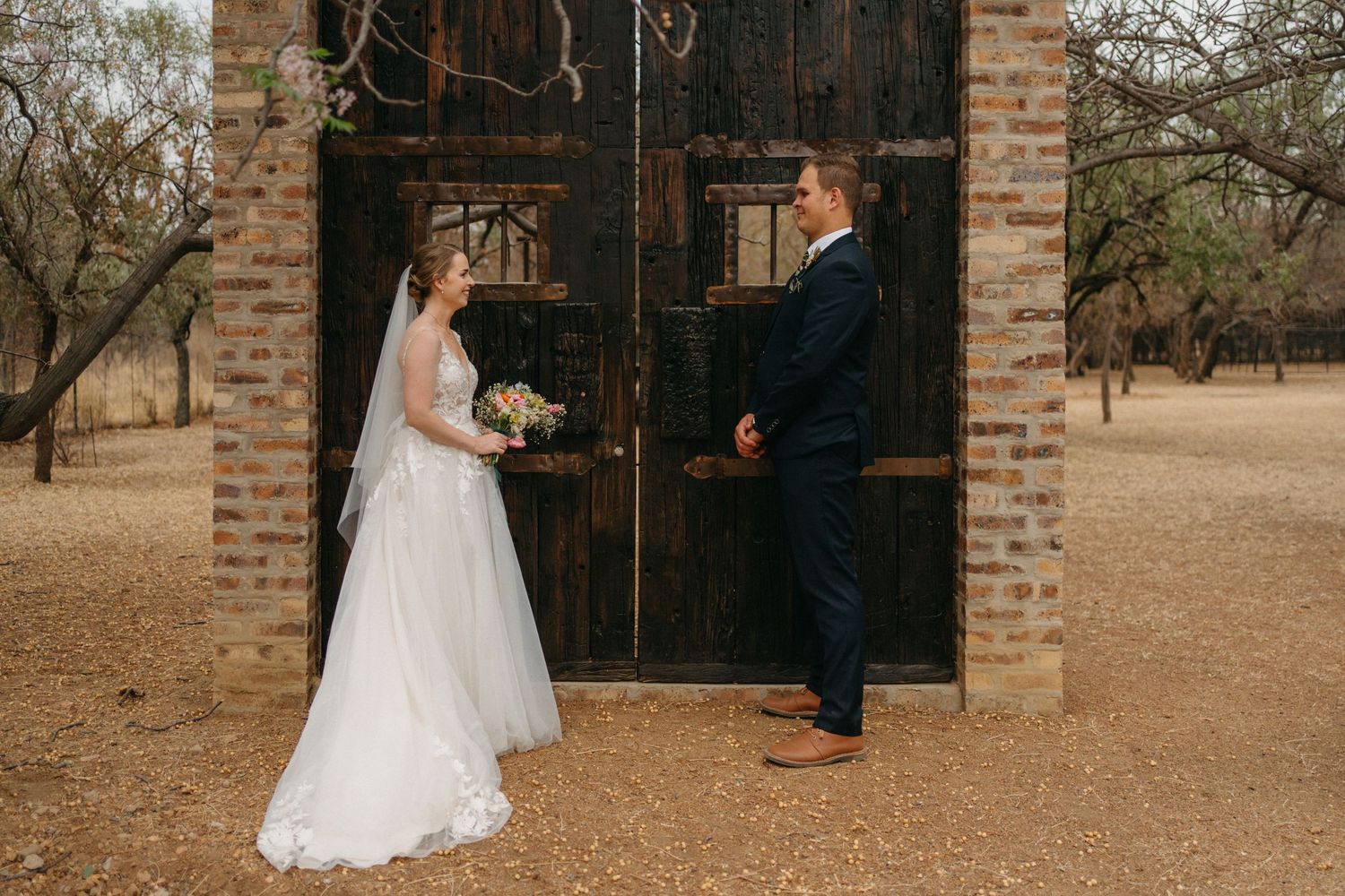 A romantic wedding moment captured at a rustic doorway made of aged brick and dark wood.
