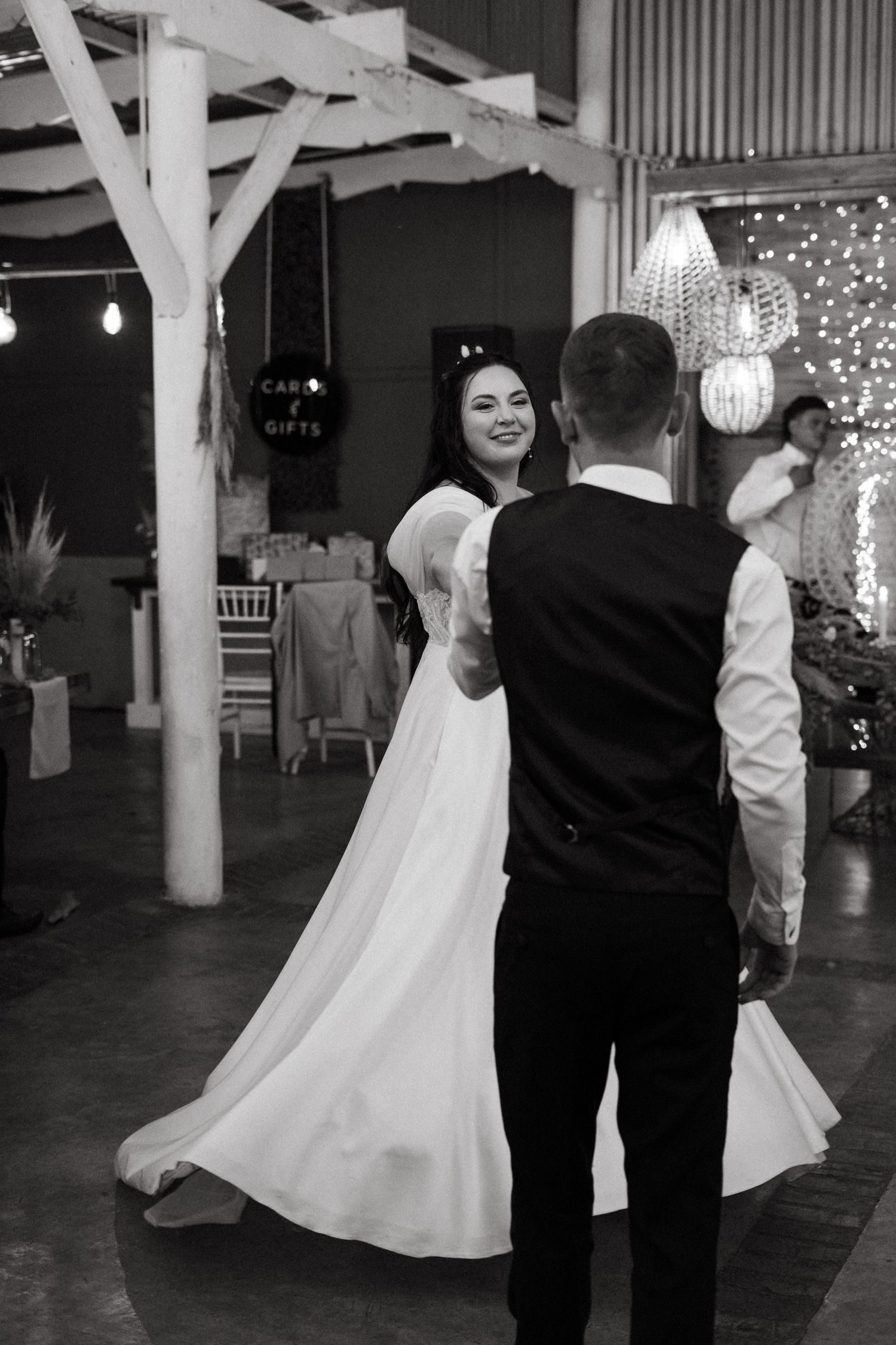 A couple dancing at a rustic wedding reception venue decorated with white posts and twinkling lights.