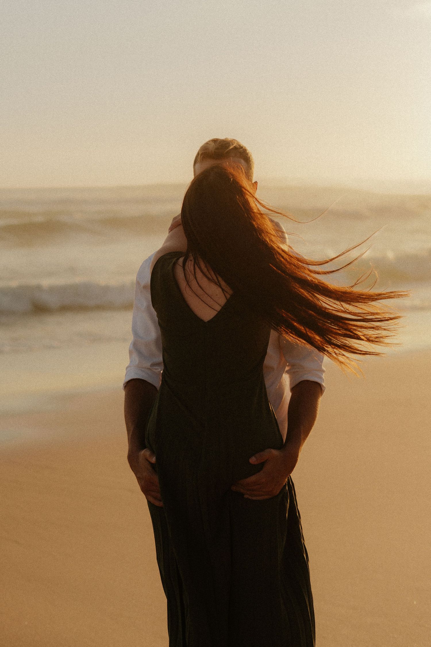 A person with long flowing hair stands on a beach in the South African Garden Route at sunset as wind blows their hair across their face.