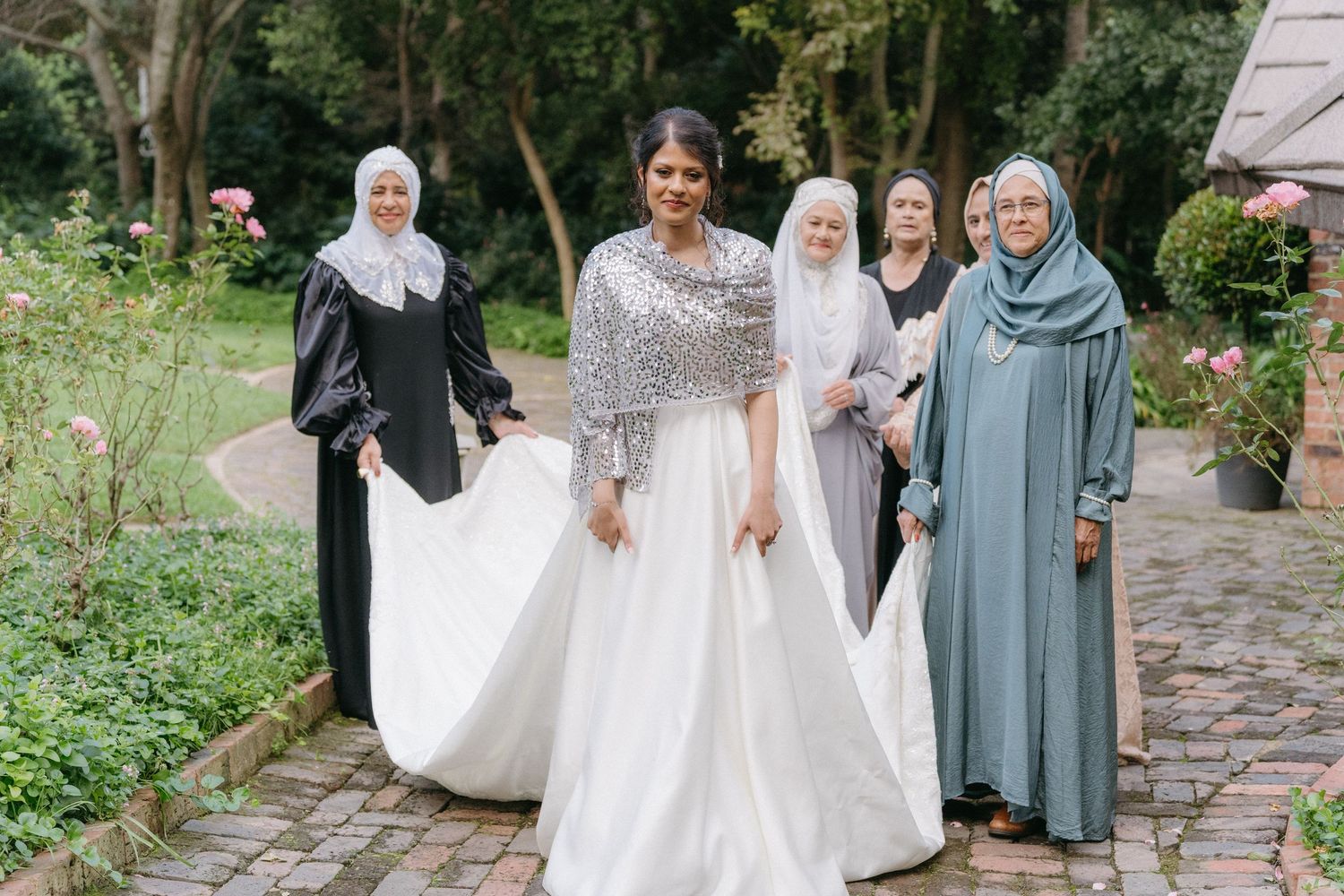 Garden wedding party photos featuring bride in white gown accompanied by guests in coordinated formal attire.