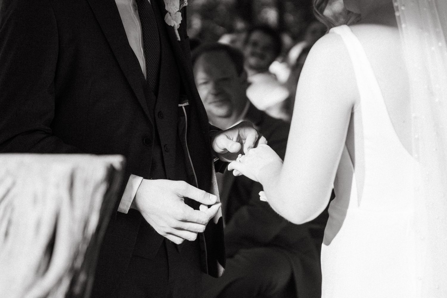 Black and white closeup of wedding couple exchanging rings during ceremony.