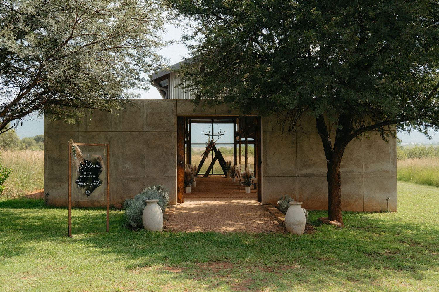 A rustic concrete entryway with trees framing a minimalist archway in an outdoor garden setting.
