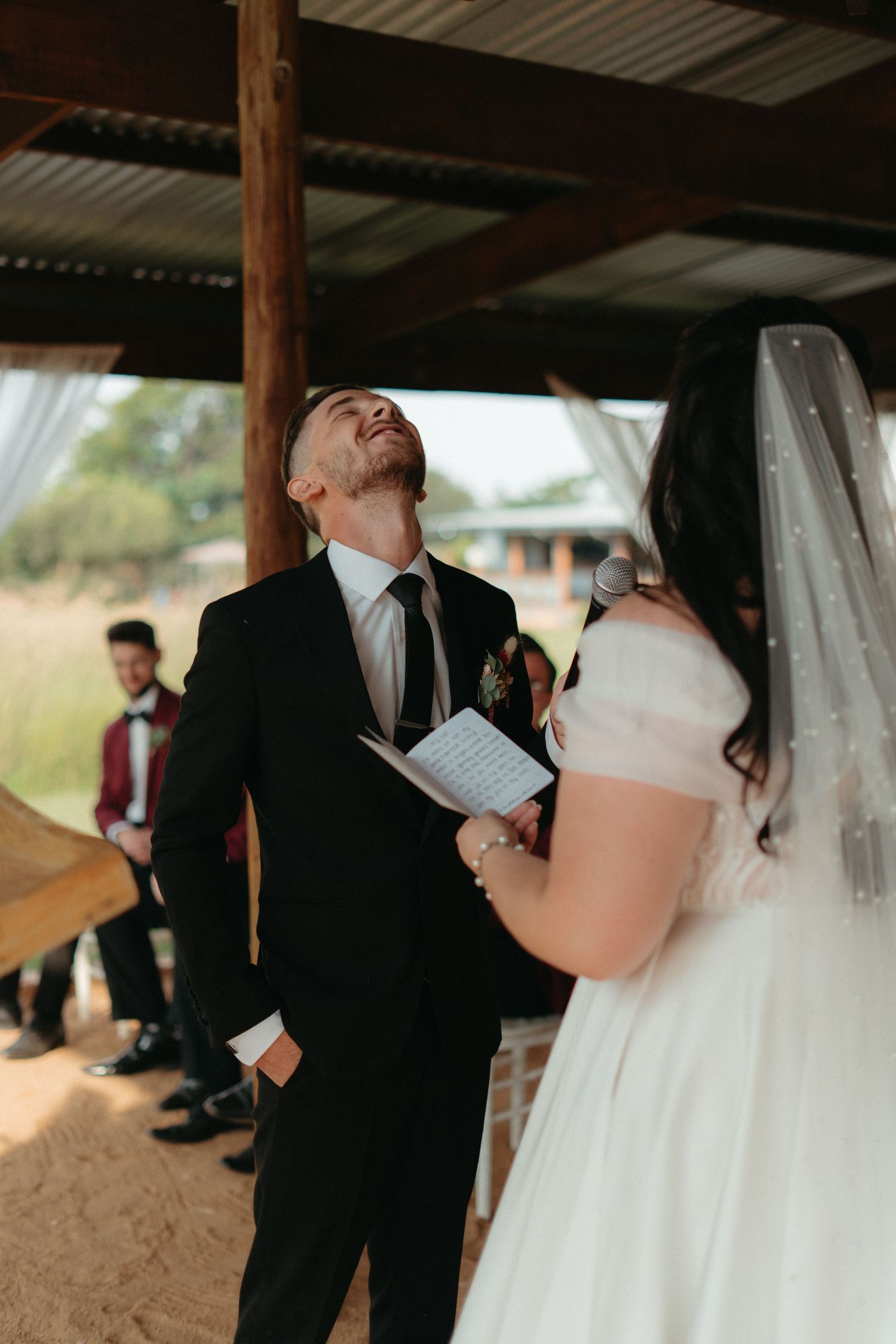 A couple sharing an emotional moment during their wedding ceremony under a rustic covered pavilion.