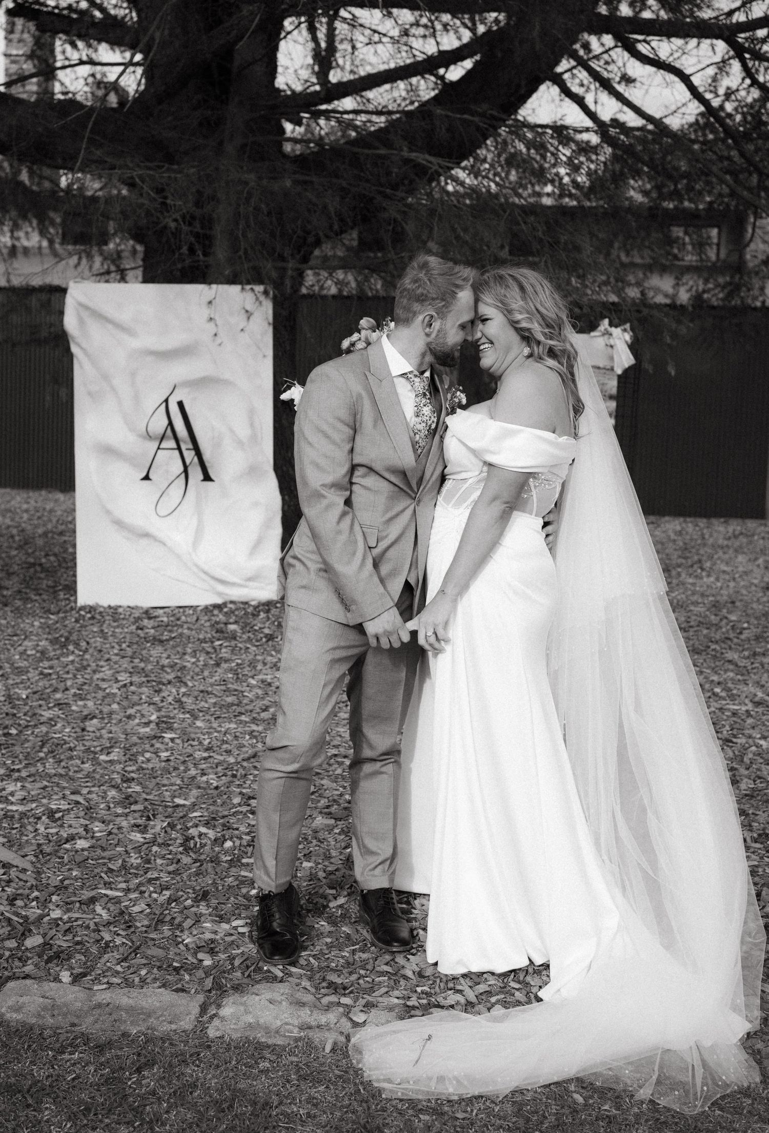 A black and white wedding photo of a couple sharing an intimate moment in front of a monogrammed banner.