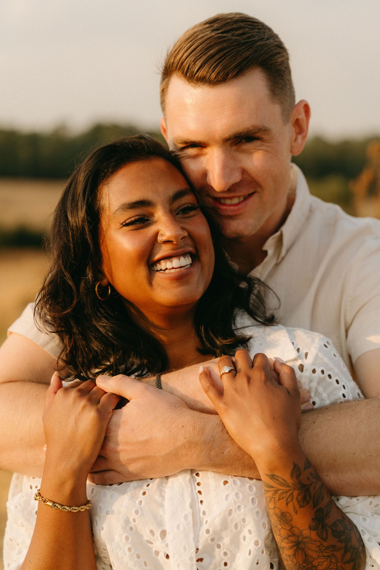 A couple embraces in a romantic outdoor photoshoot during golden hour wearing white clothing.
