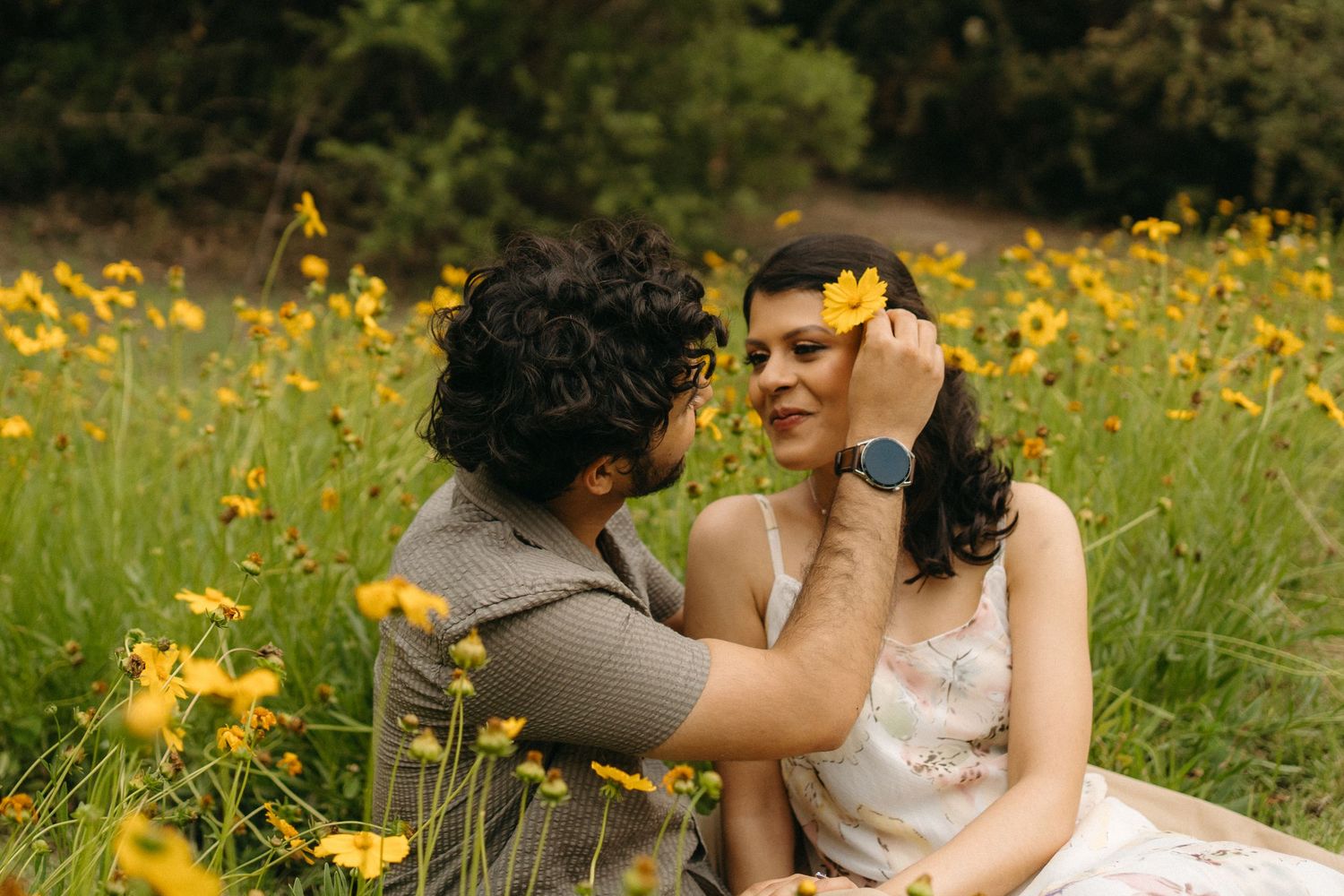 Two people share a tender moment in a meadow of yellow wildflowers on a sunny summer day.