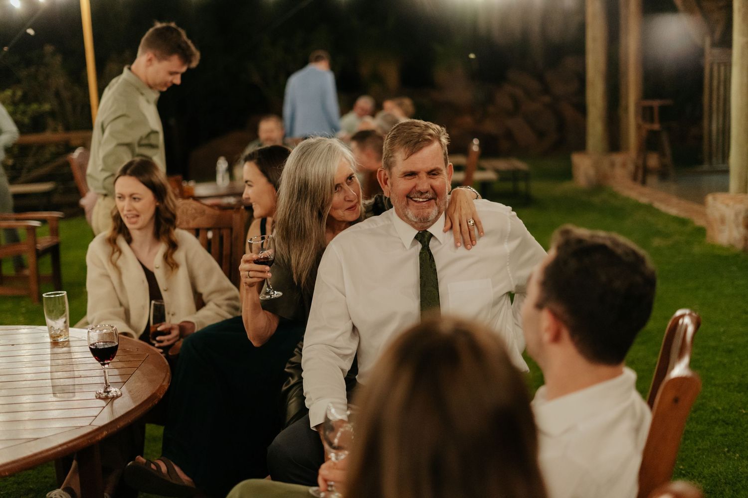 Wedding guests enjoying conversation and drinks during an outdoor evening reception.