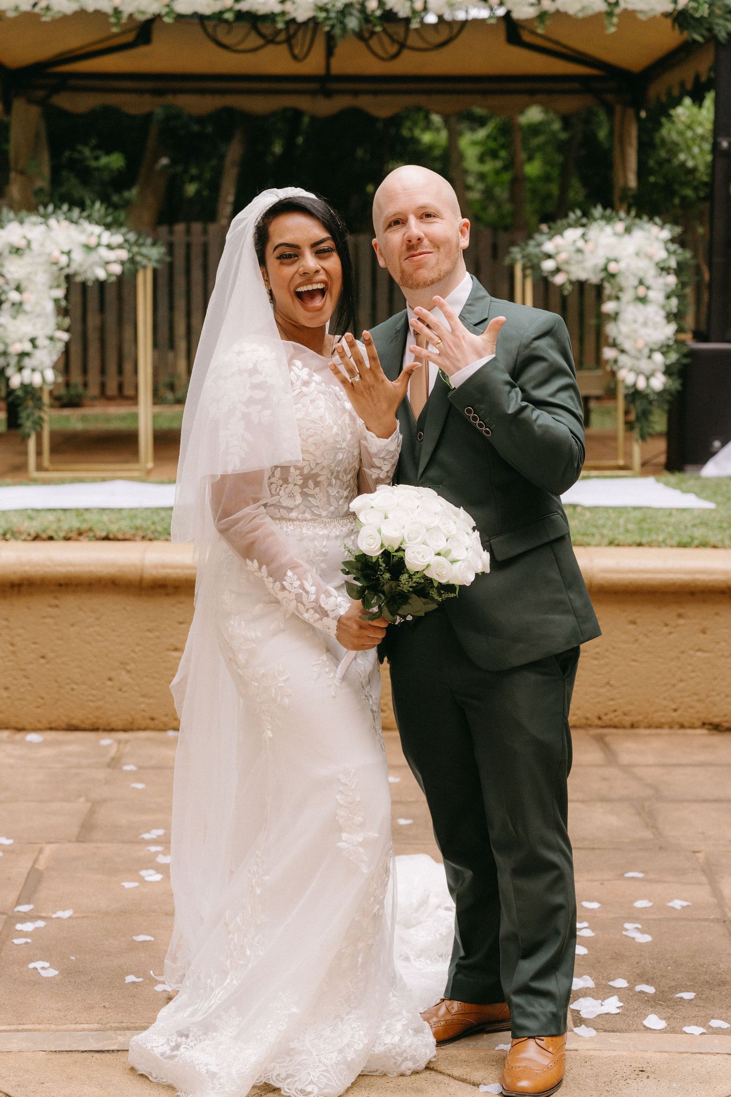 A joyful moment at an outdoor wedding ceremony as newlyweds show off their rings beneath a decorative gazebo.