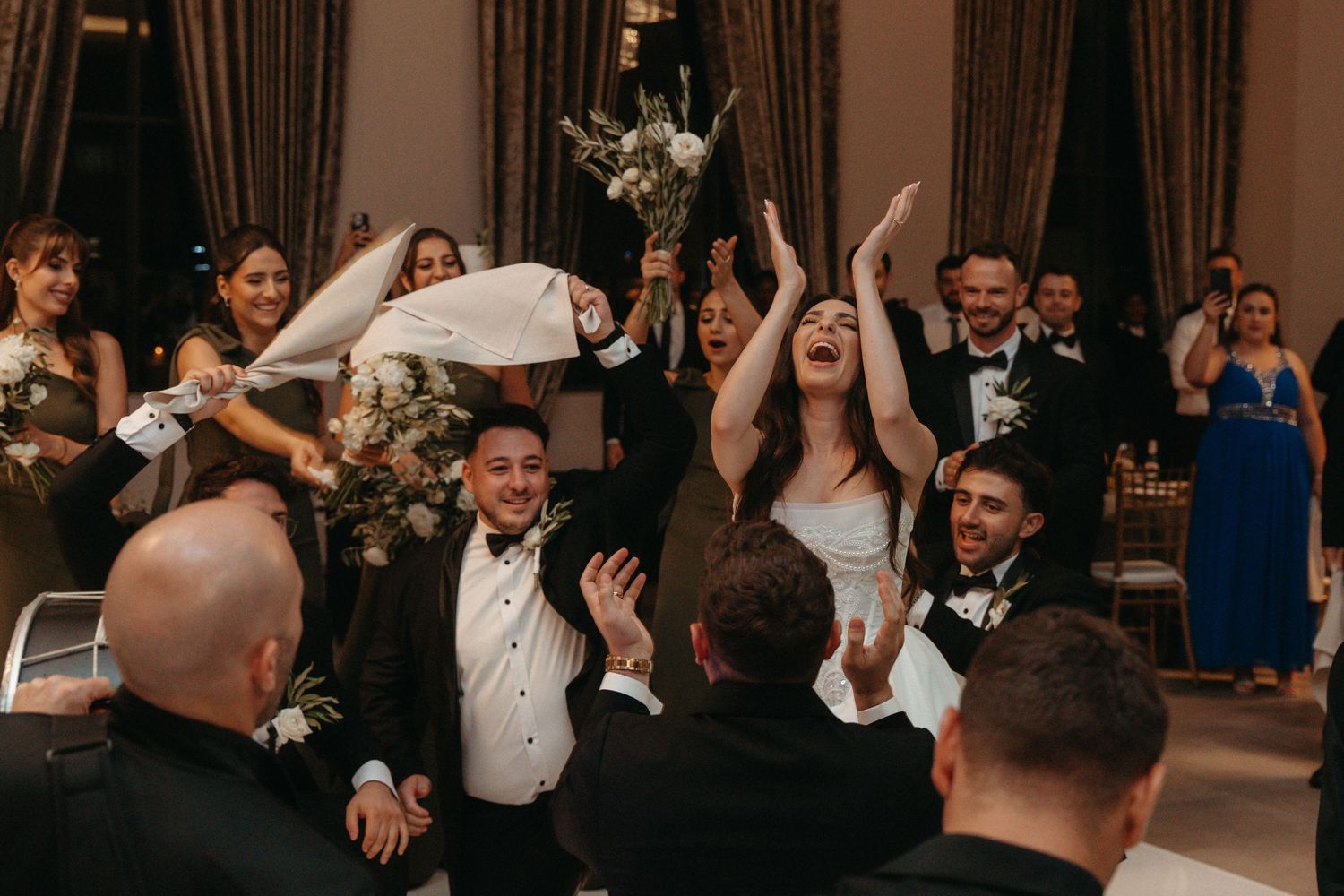 Joyful wedding reception entrance with bride and groom celebrating alongside bridal party in elegant ballroom.