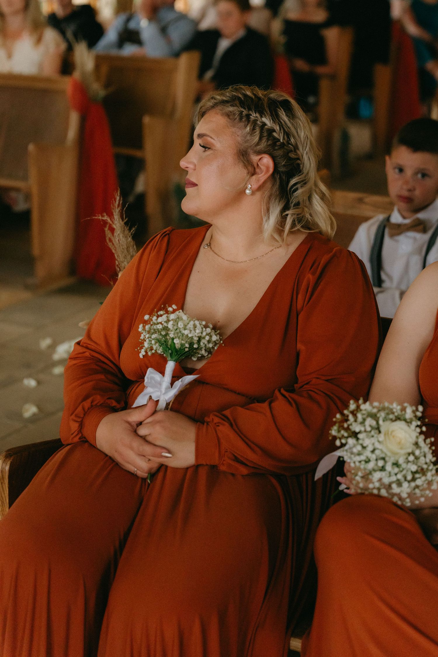 Bridesmaids in burgundy dresses sit together during wedding ceremony.