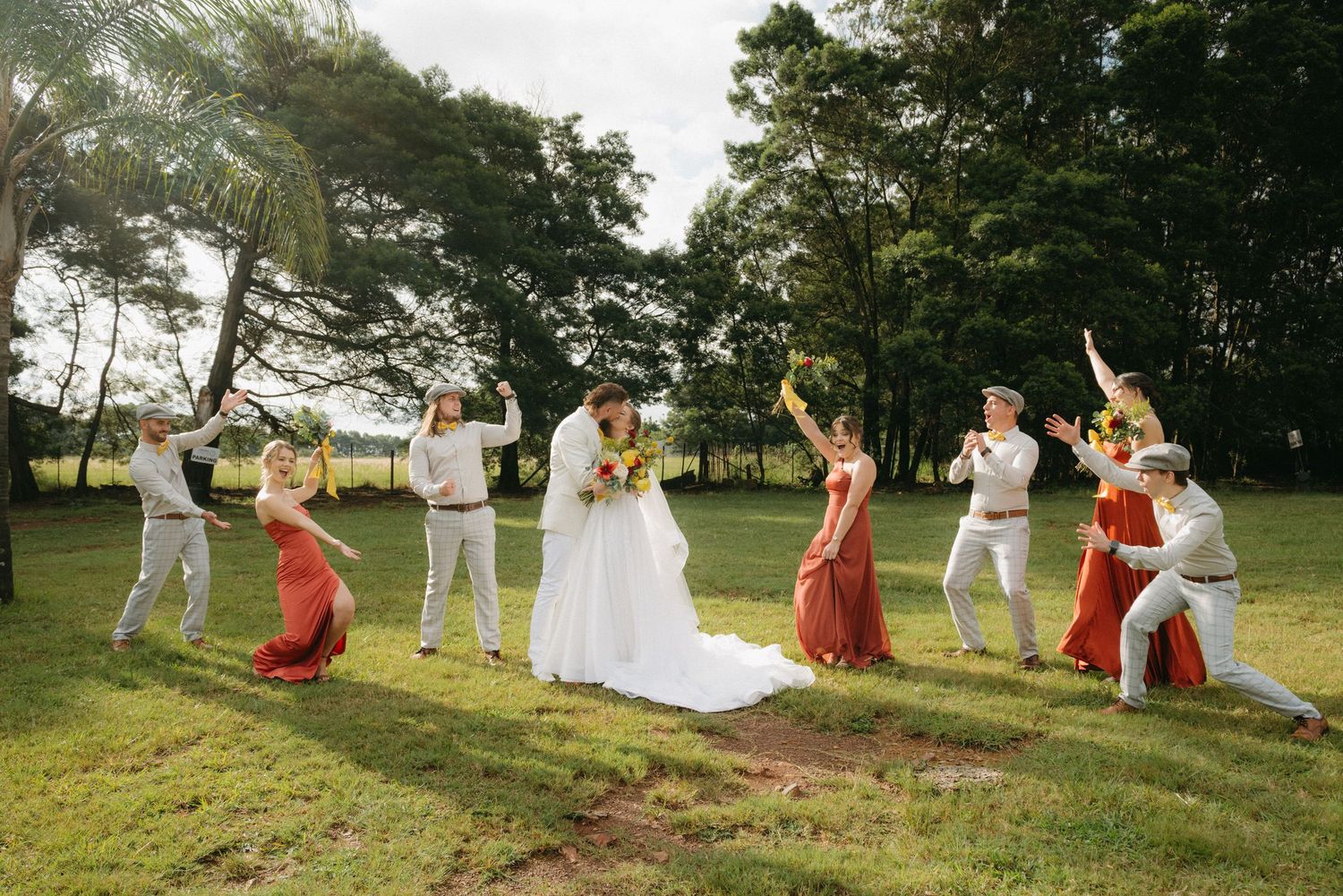 Wedding party strikes fun poses on grassy field during sunset photo session.