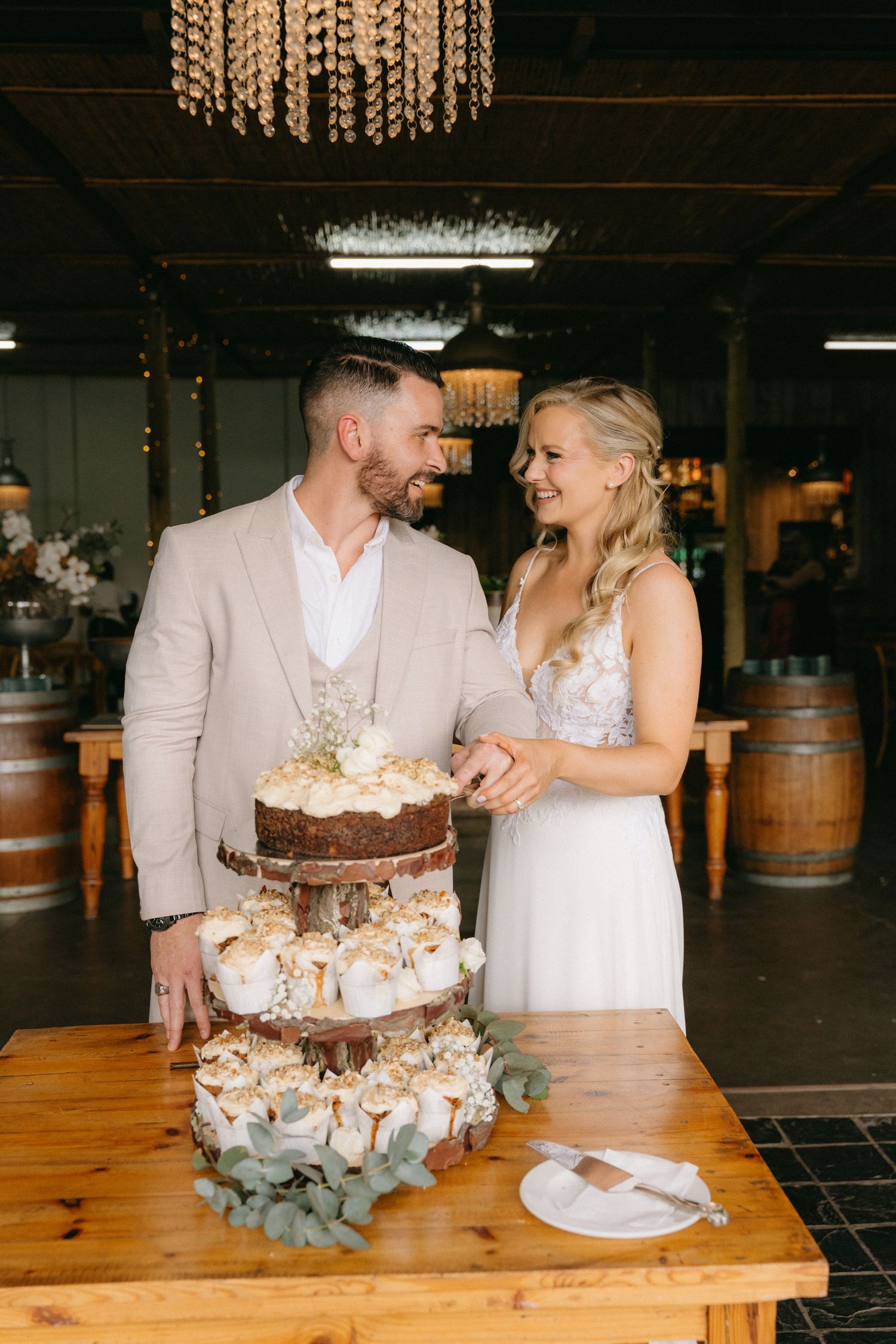 Newlyweds share a playful moment while cutting their tiered wedding cake.