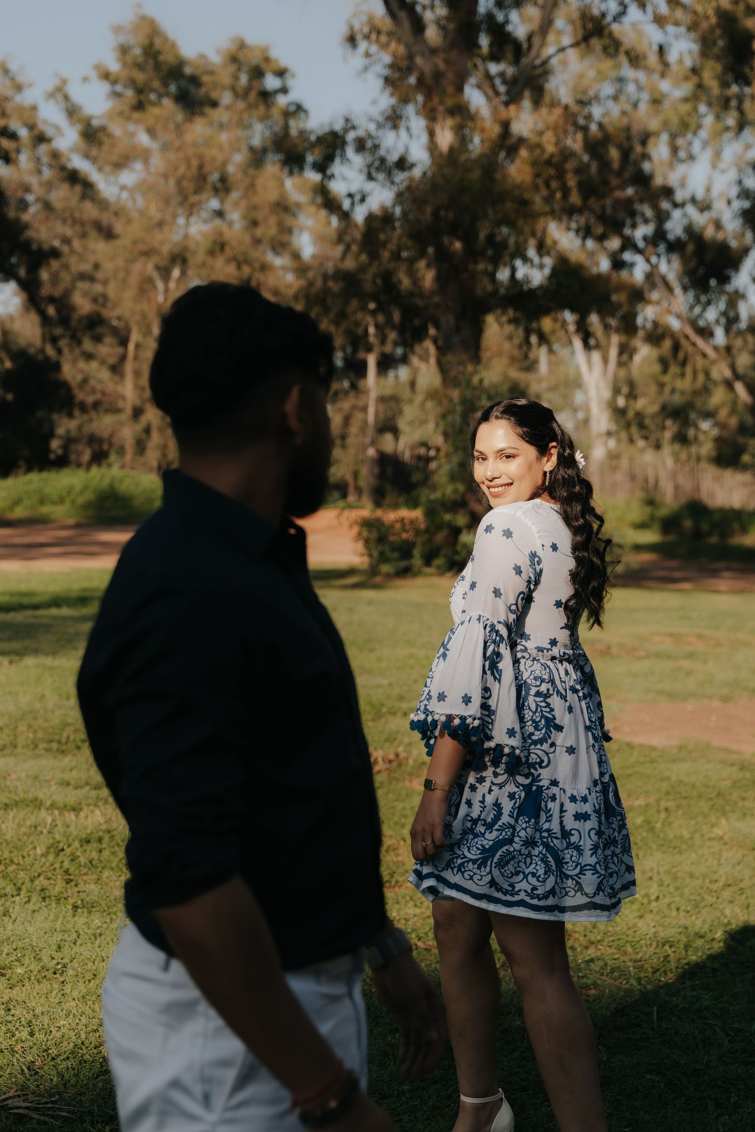 A couple walks together through a sunlit park on a warm autumn day, with golden trees in the background.