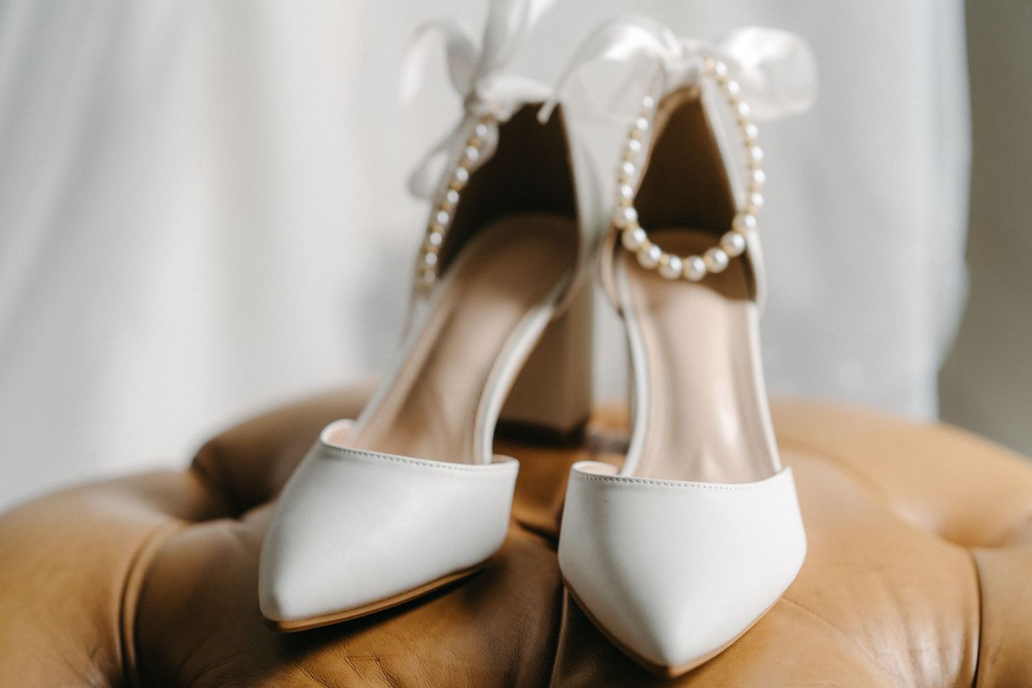 Elegant white bridal shoes with pearl details and ribbon ties on leather surface.