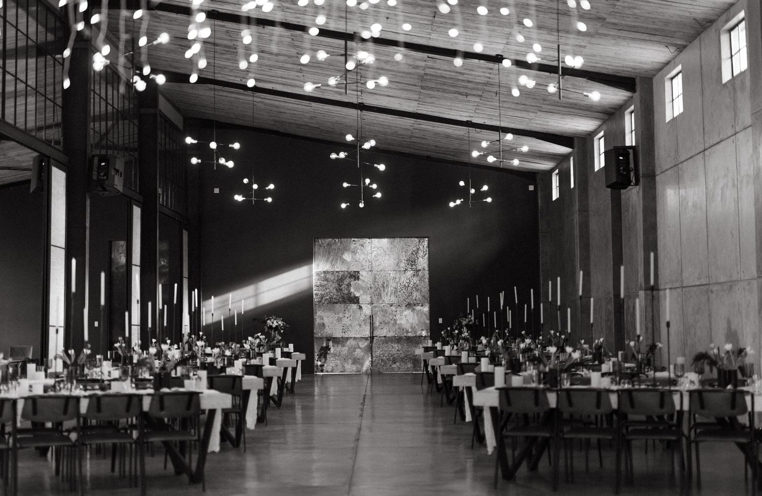 An elegant banquet hall decorated with string lights and long tables set for a formal event in black and white vintage style.