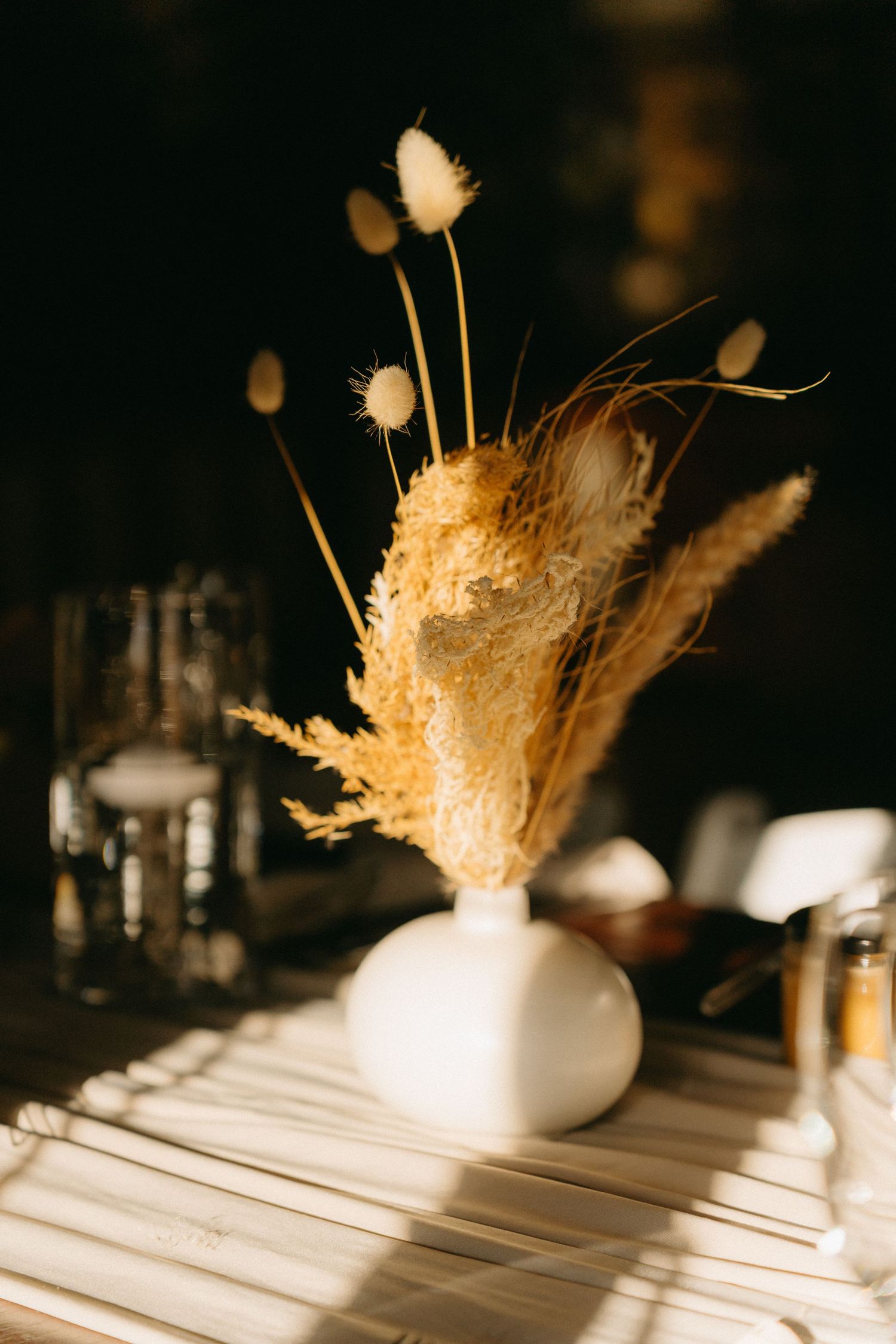 Decorative dried pampas grass arrangements in white vases on a table create an elegant minimalist centerpiece display.