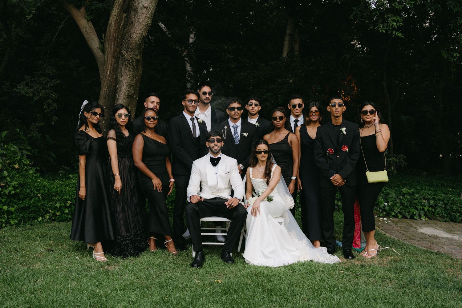 Wedding party poses outdoors with couple in center surrounded by attendants in black attire.