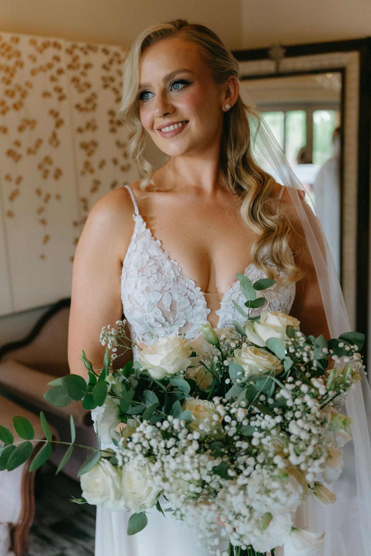 White bridal bouquet with roses, eucalyptus, and baby's breath against floral wallpaper.