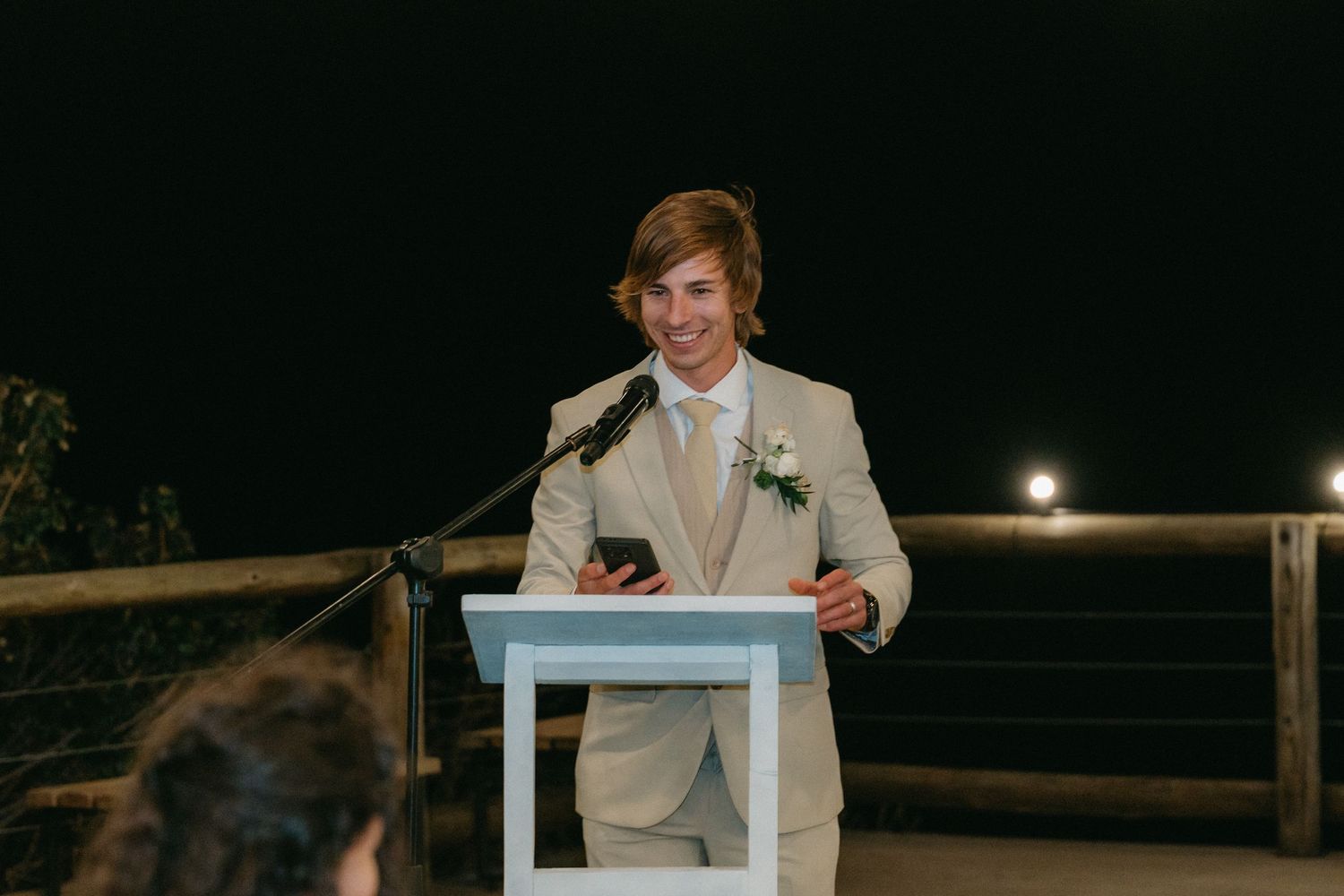 Evening wedding reception speech at outdoor venue with rustic wooden details.
