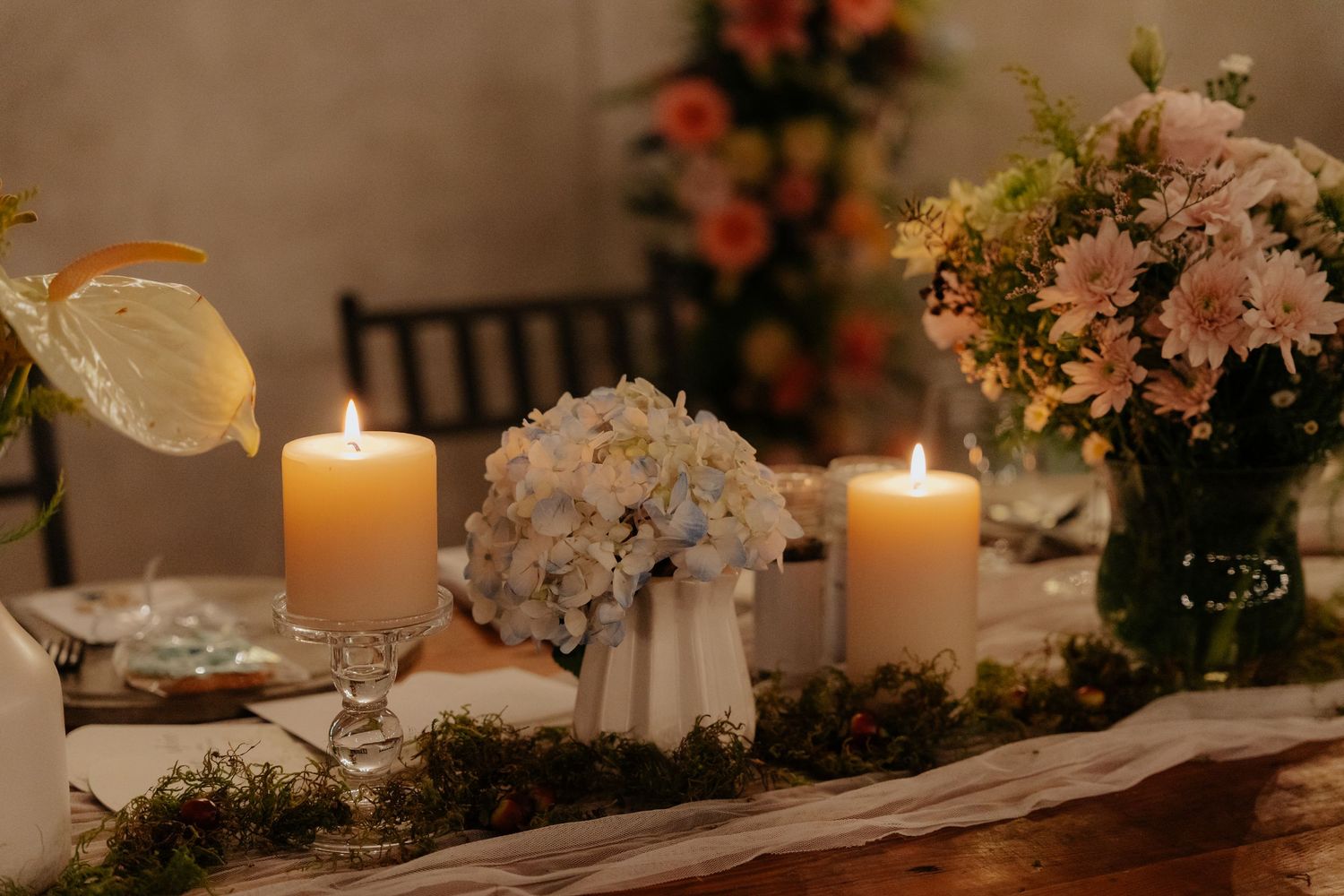 Romantic table setting with glowing candles, white hydrangeas, and pink floral arrangements in a dimly lit room.