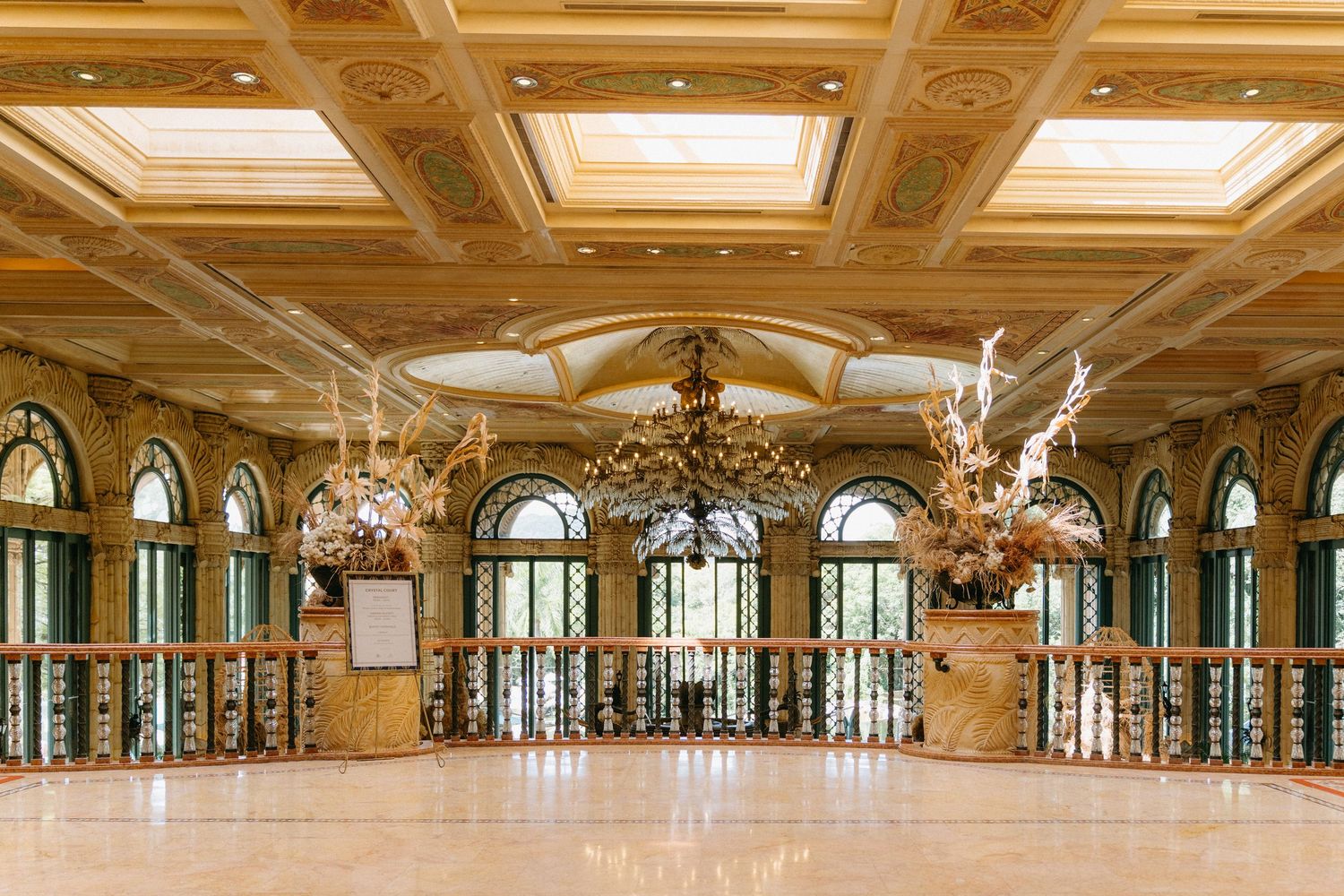 Elegant grand ballroom with ornate coffered ceiling, crystal chandeliers, and arched windows in a luxury hotel or palace.