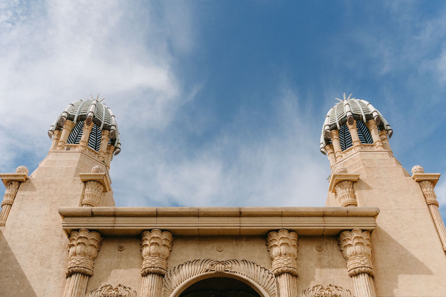 Looking up at ornate twin towers with Spanish colonial architectural details against a blue cloudy sky.