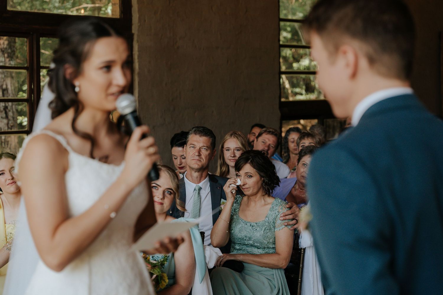 A couple shares an intimate moment during their wedding ceremony while guests look on in the background.