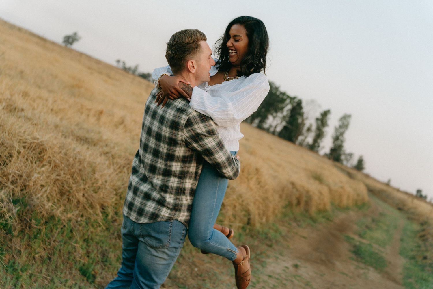 Couple dancing and spinning together in a golden field at sunset wearing casual clothes.