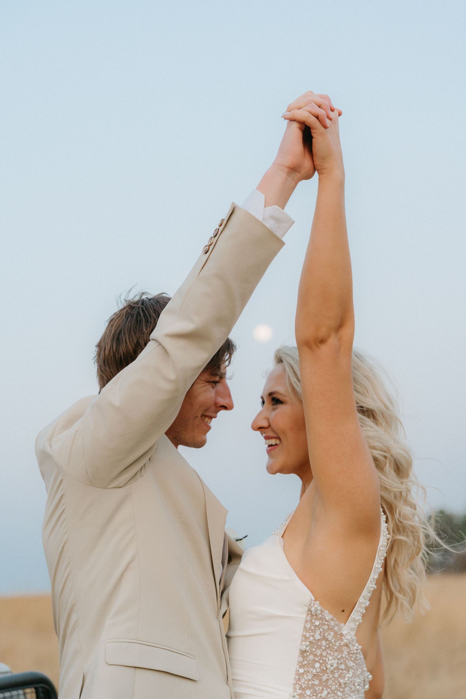 Dancing couple shares a joyful moment at sunset in formal wedding attire.