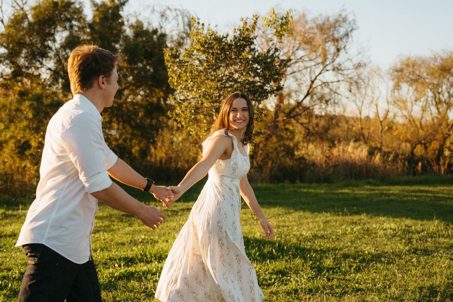 A couple dances together in a lush grassy field at golden hour, with the bride wearing a flowing white lace dress.