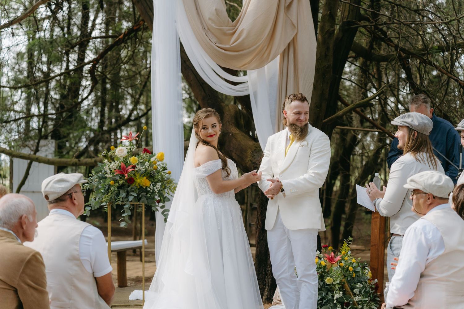 Outdoor wedding ceremony under draped fabric with sunflowers and natural greenery.