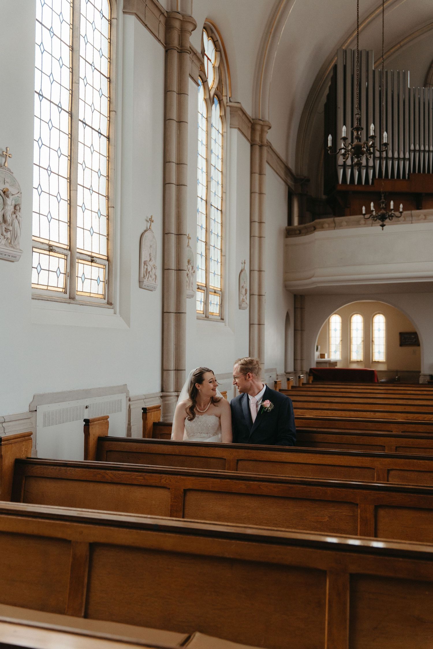 Interior of a traditional church with wooden pews, tall windows, and a pipe organ visible in the balcony area.
