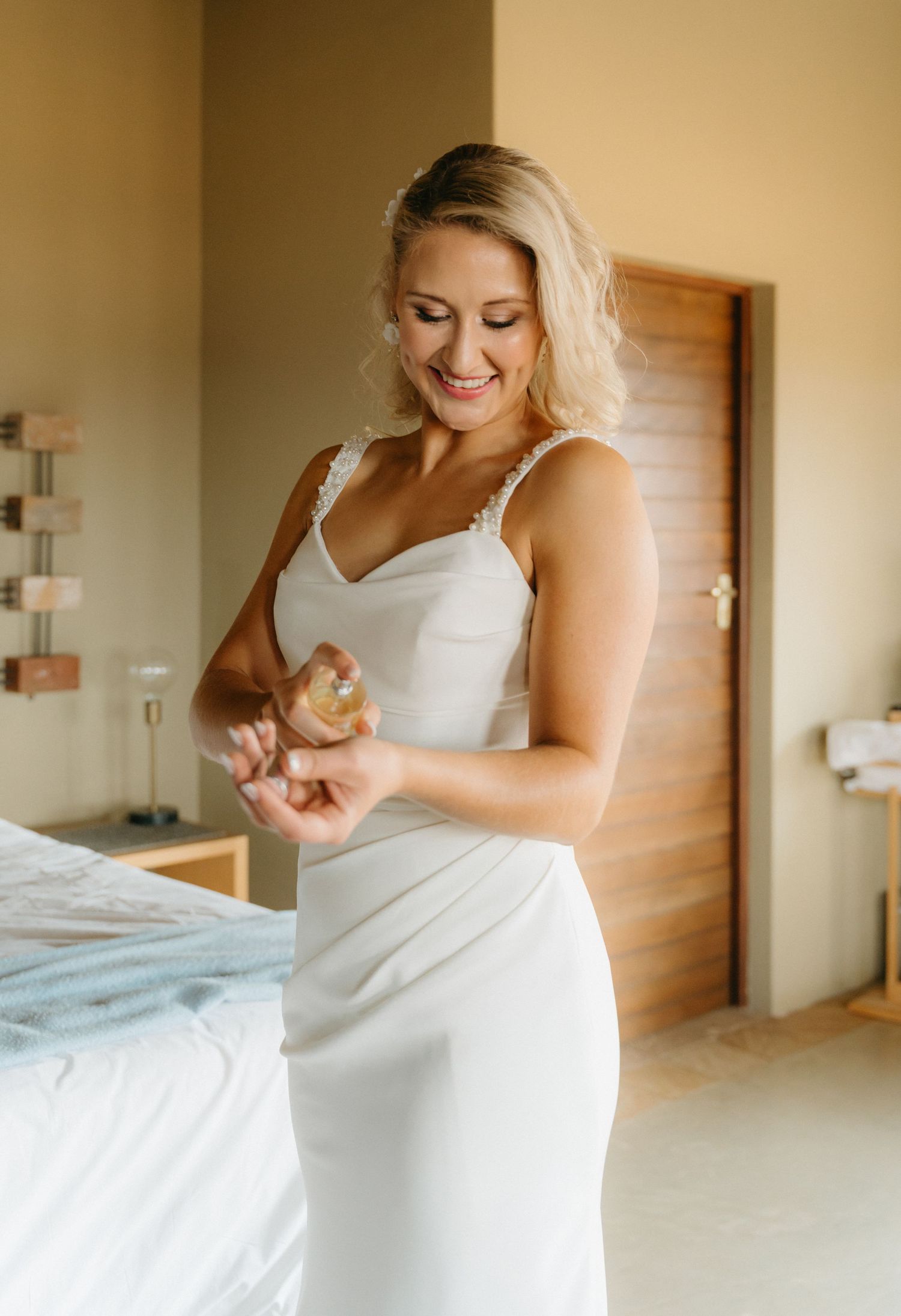 A wedding dress being fitted and adjusted in a sunlit room with warm beige walls.