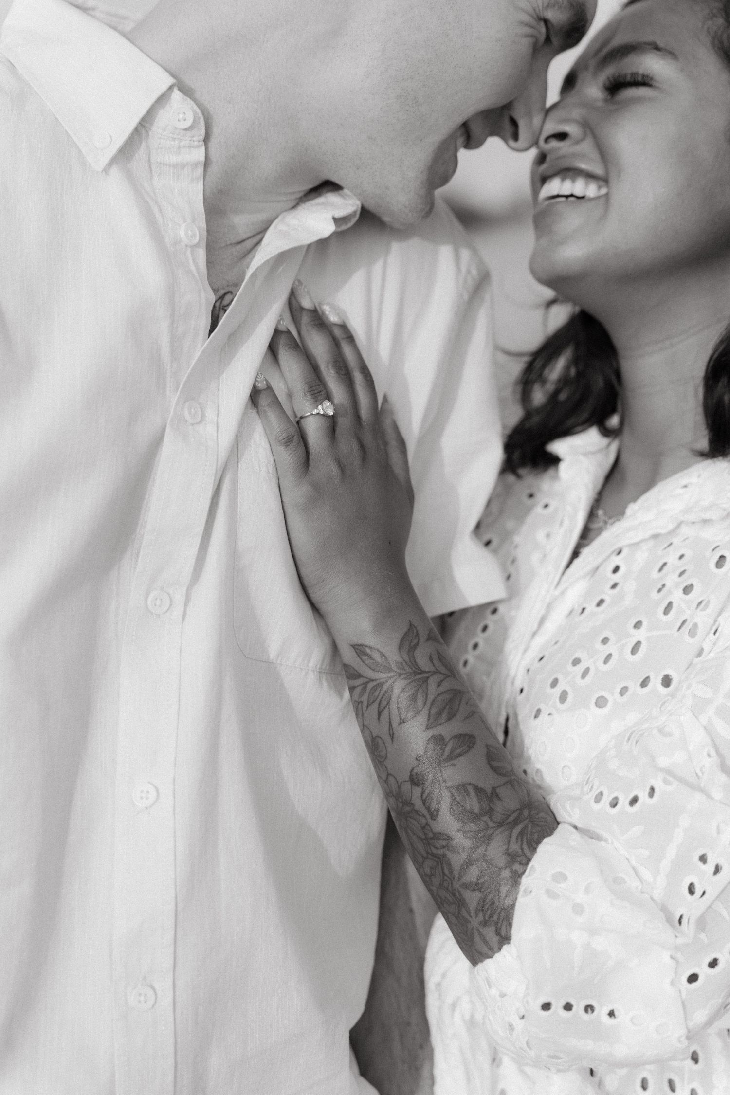 Black and white close-up of a laughing woman with an engagement ring embracing her partner.