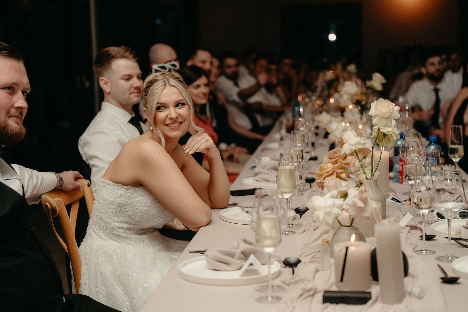 Wedding guests seated at elegantly decorated tables with white floral centerpieces during an indoor reception.